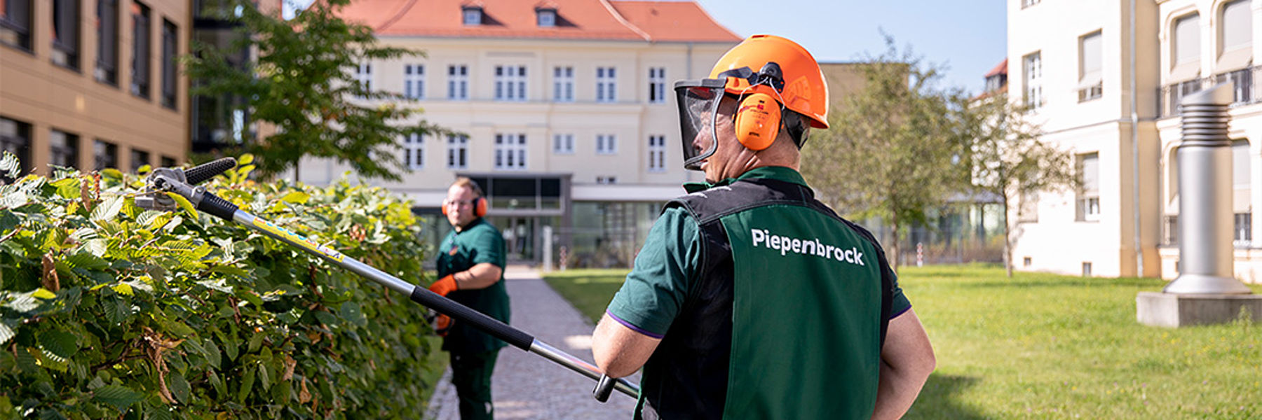 Piepenbrock-Mitarbeiter schneidet mit Heckenschere eine Grünanlage